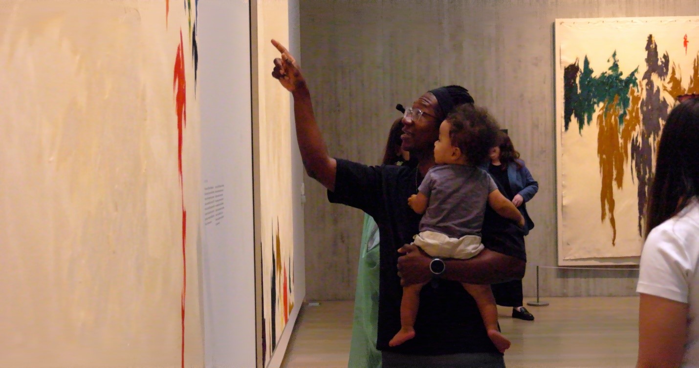 A person holding a baby pointing at a paintingAI-generated content may be incorrect., Picture